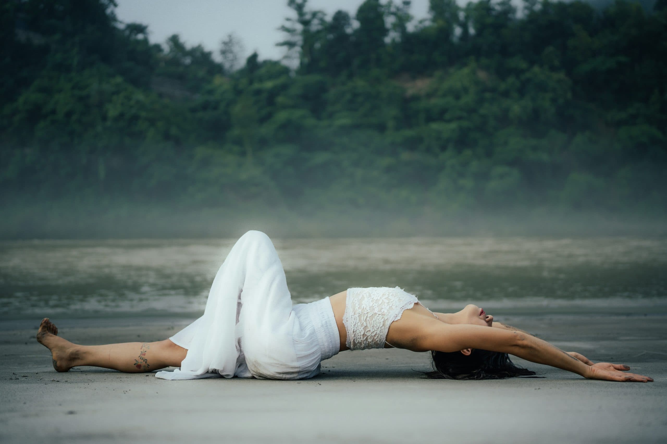 A woman resting in a calm, restorative stretch on a misty shoreline